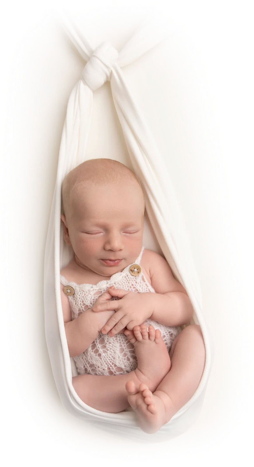 A newborn sleeping in a soft white hammock wrap