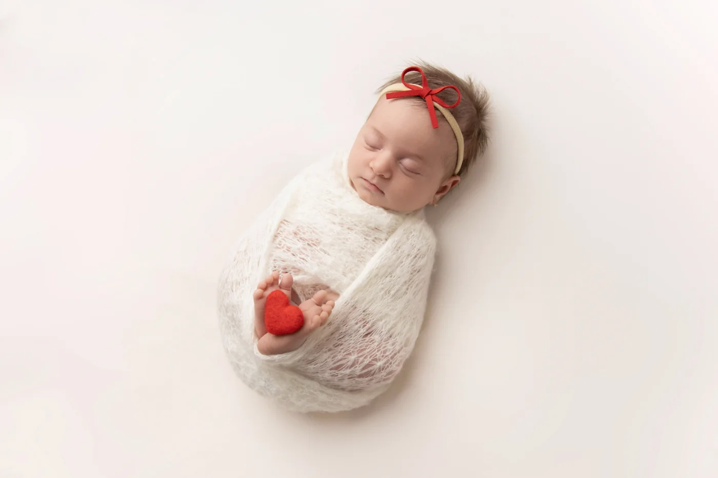 Newborn in a red bow holding a small red felt heart