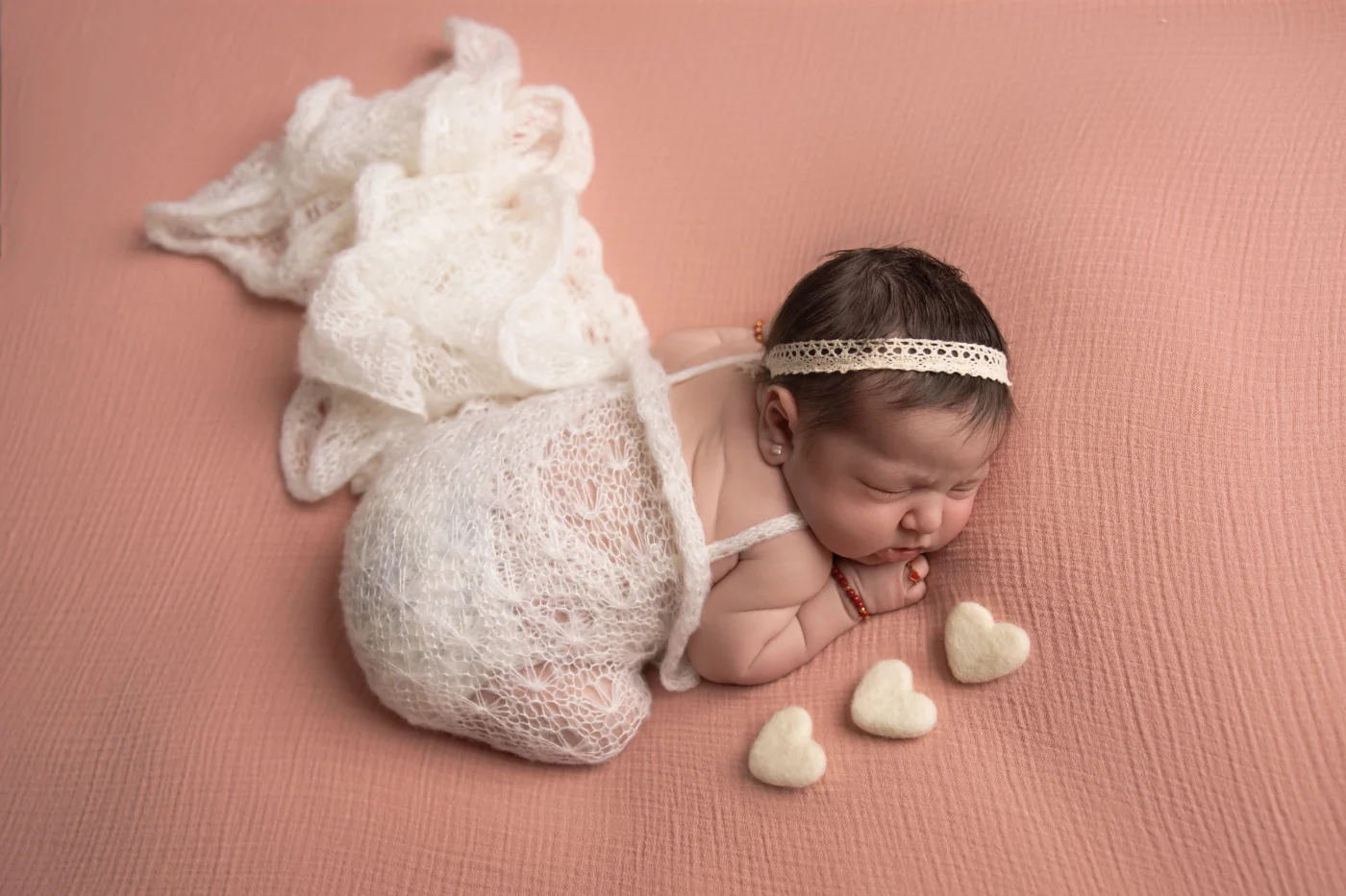 Newborn nestled beside a soft doll and knit bunny
