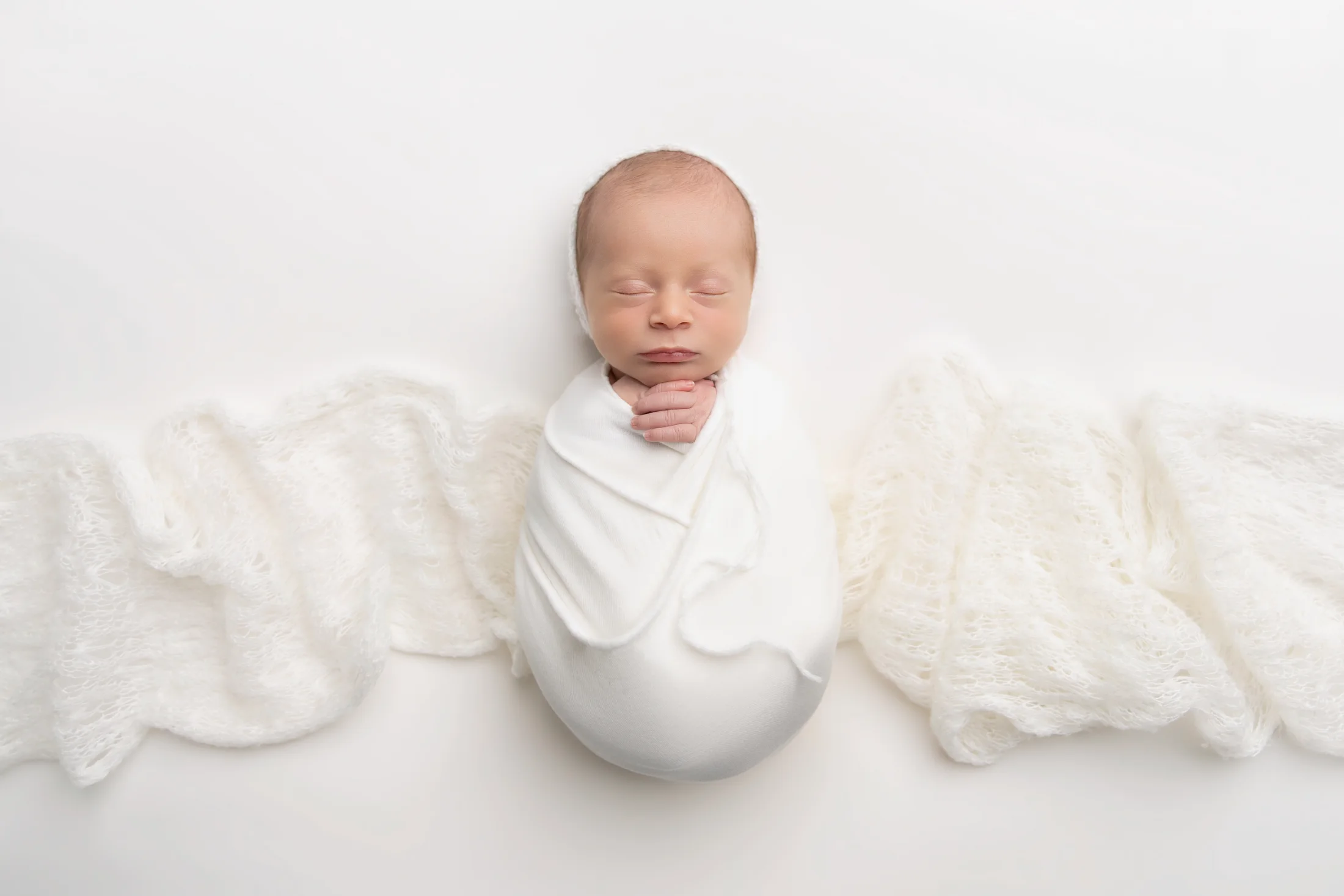 A peacefully sleeping newborn nestled in soft white wraps