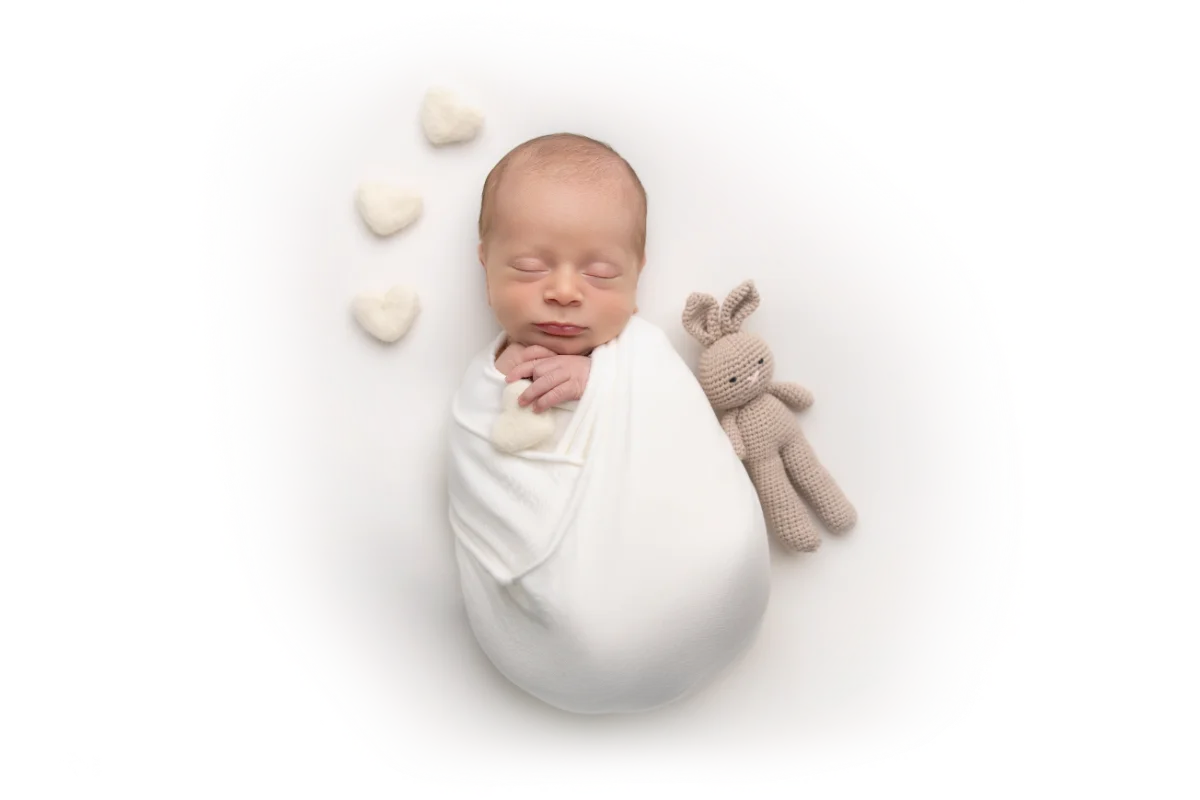 A newborn in a soft blue knit bonnet, swaddled in cream beside felt hearts