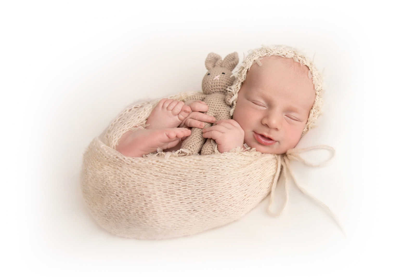 A sleeping newborn wearing a small red bow, resting on folded hands