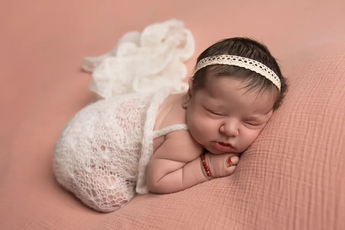 Newborn girl with a lace headband asleep on a dusty pink blanket — newborn photography by Gitty Reiss, Boro Park, Brooklyn